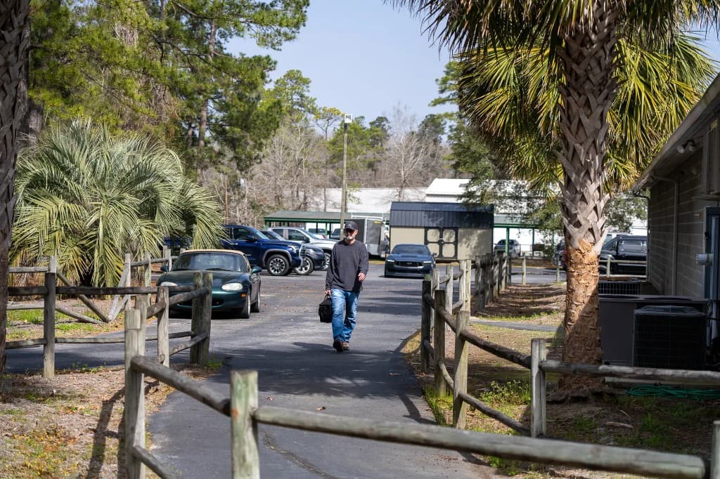 Guest walking toward Lowcountry Guns along the fenced entrance path, parking and trees in the background